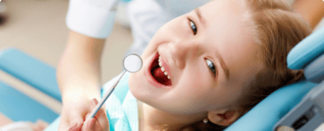 A young girl smiles while being examined by a dentist.