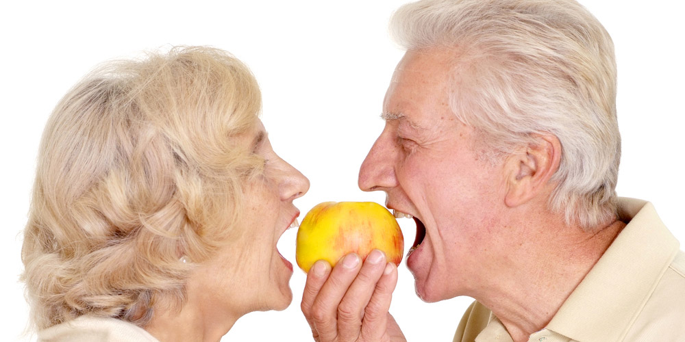 An older couple eating an apple.