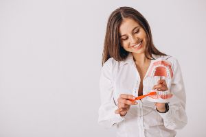 A woman in a white shirt is holding a model of a tooth.