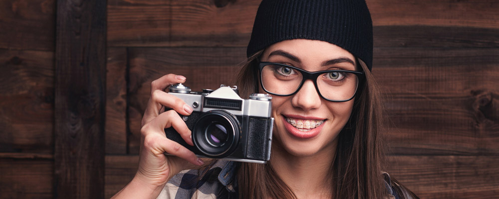 A woman wearing glasses is holding a camera.