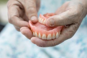 A woman holding a denture in her hands.