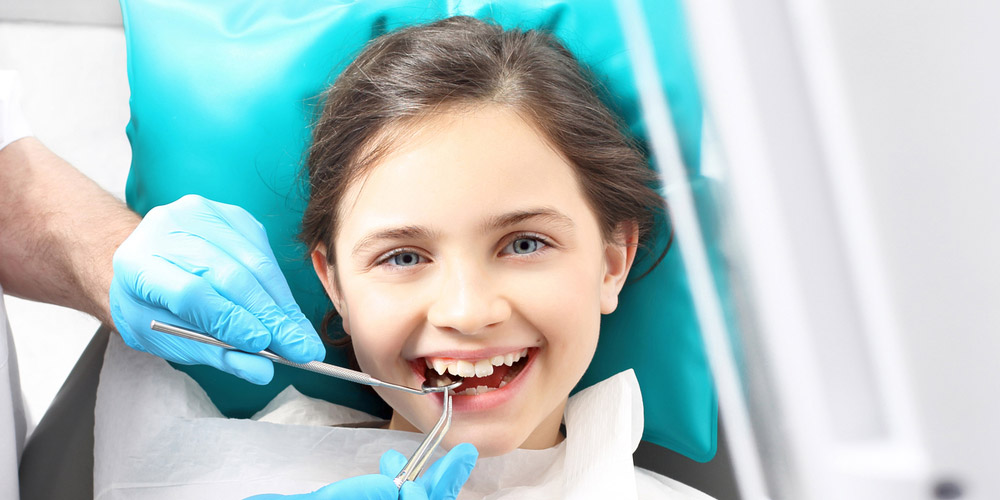 A young girl is getting her teeth checked by a dentist.