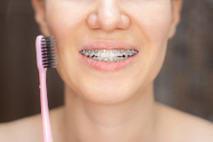 A woman is brushing her teeth with a pink toothbrush.