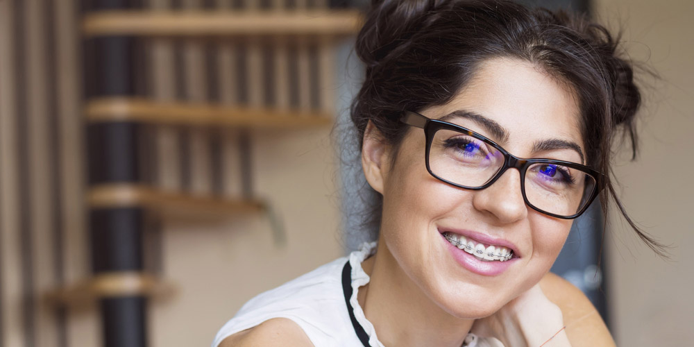 A woman in glasses smiling while sitting on a chair.