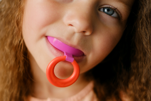 A little girl with a pink and purple ring in her mouth.