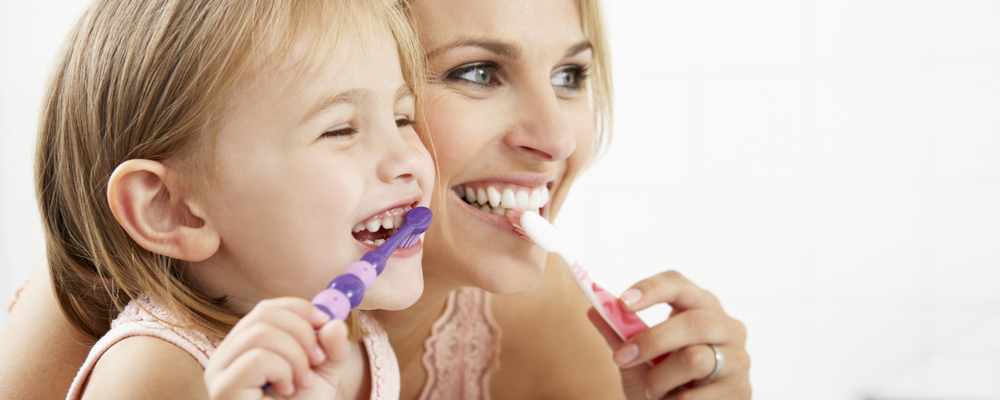 A mother and child brushing their teeth together.