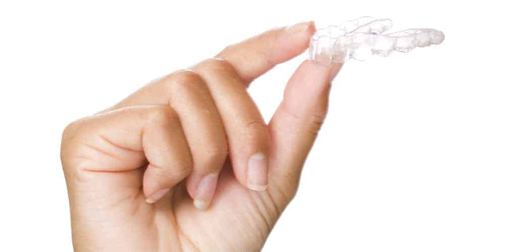 A person's hand holding a clear aligner.