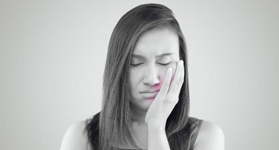 A woman with her eyes closed holding her cheek.