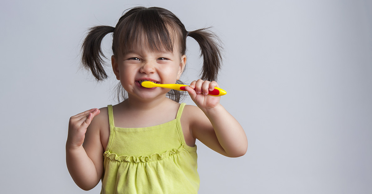 A girl with pig tails holding a toothbrush in her mouth.